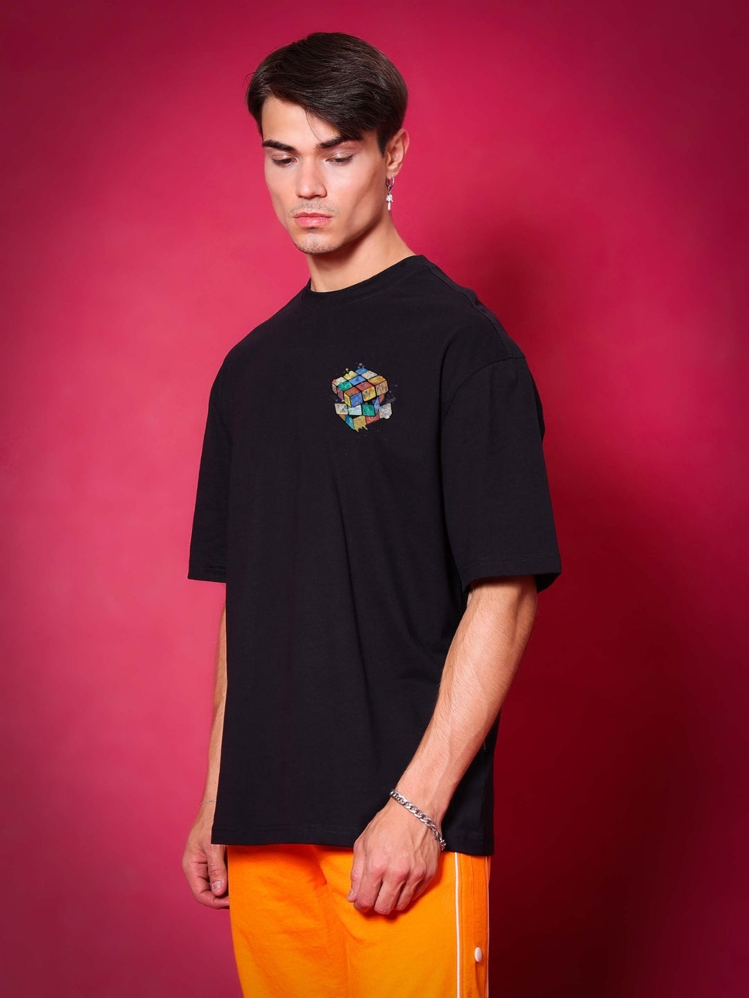 Model wearing RUBIK REVOLUTION OVERSIZED T-SHIRT BLACK with a colorful graphic on a vibrant background.