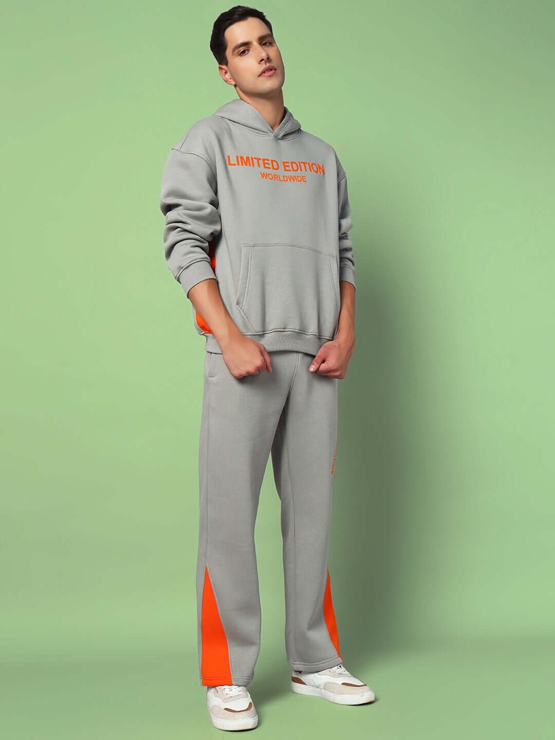Model wearing grey Worldwide Cotton Fleece Jogger with orange accents, standing on a light green background, showcasing casual style.