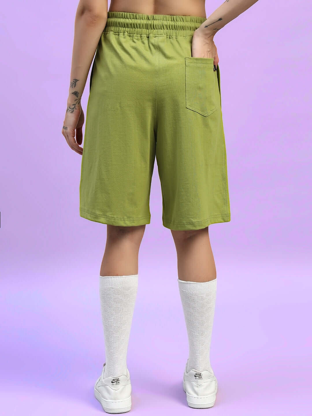 Back view of women's olive green wideline regular fit shorts with pocket, styled with white socks and sneakers.
