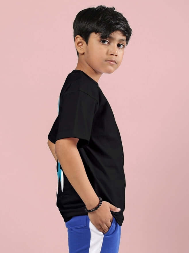 Boy wearing black Tiny Toon printed t-shirt, side view, on pink background.