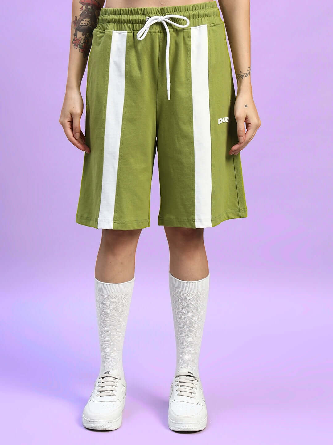 Women's olive green wide-leg shorts with white vertical stripes and drawstring waist, showcased with white sneakers and socks.