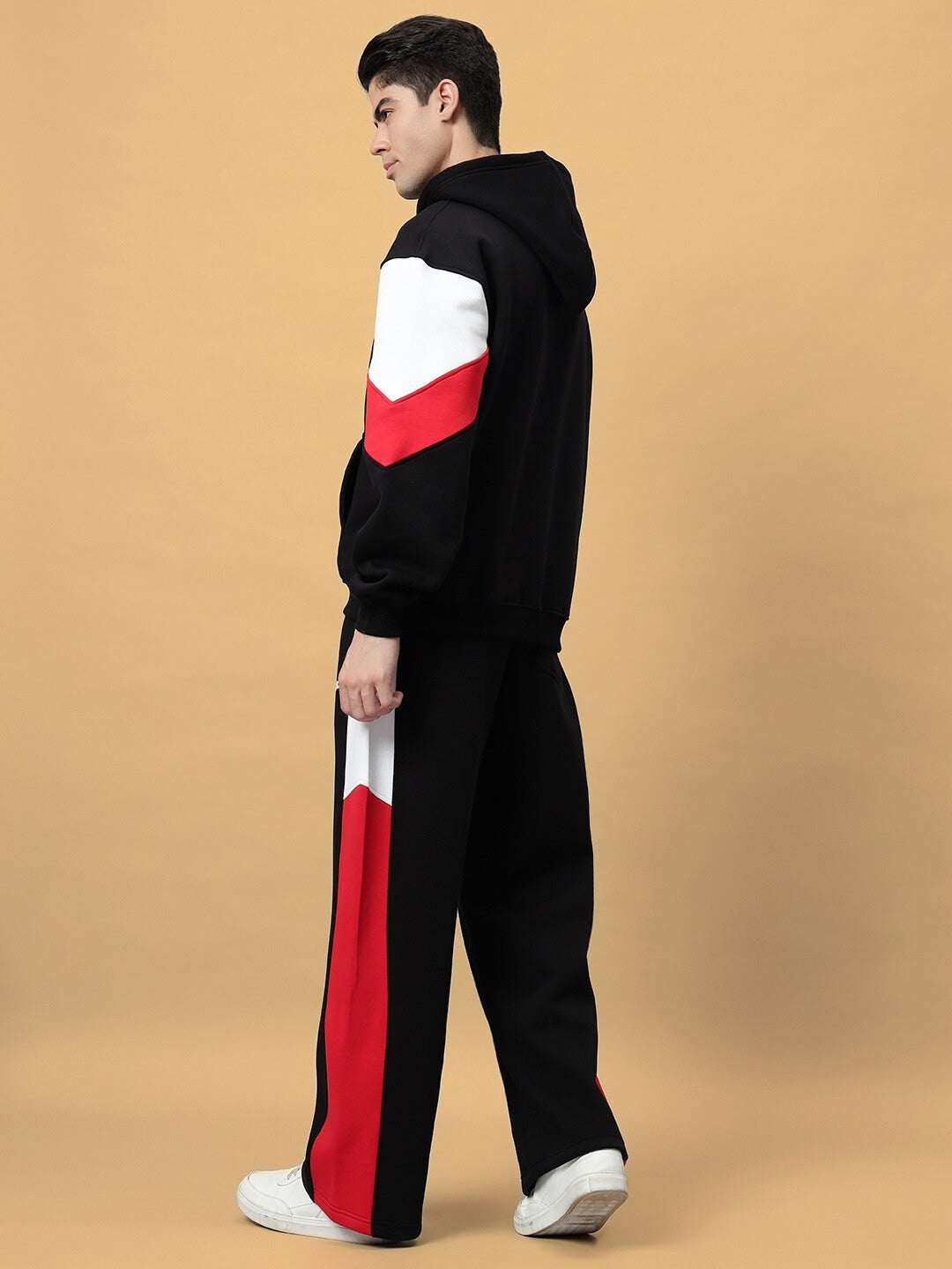 Man wearing BRIO fleece colorblock co-ord in black with red and white accents, standing sideways on a beige background.