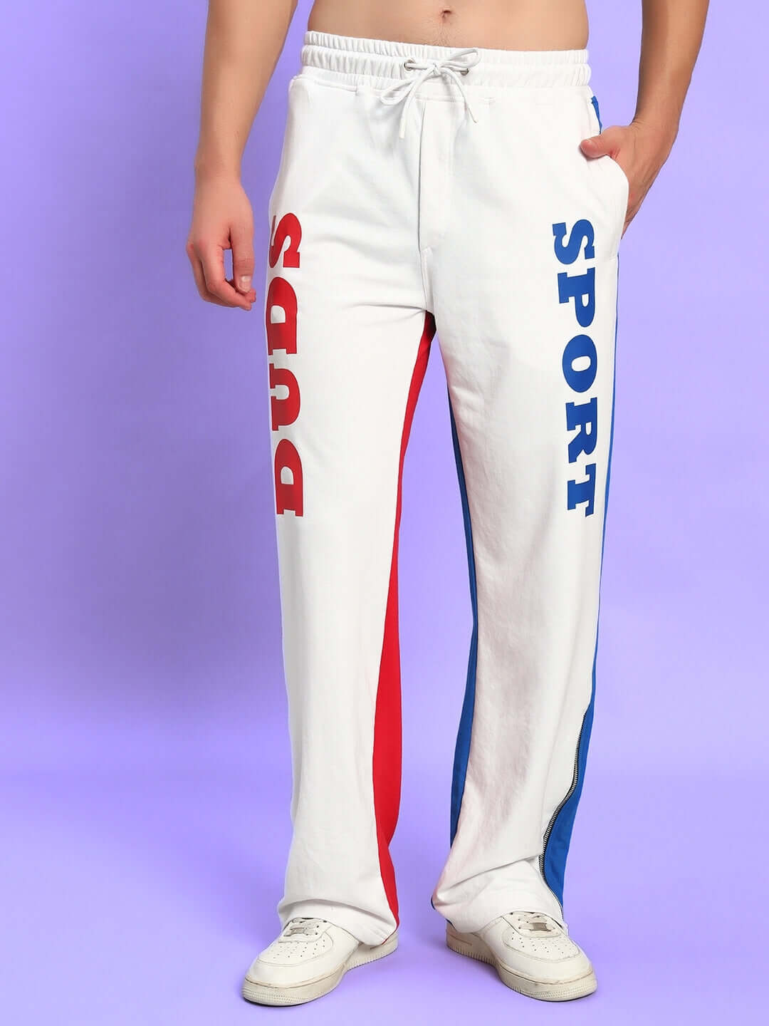 White track pants with red and blue side panels, featuring bold "SPORT" and "PUDS" lettering, modeled in a relaxed fit.