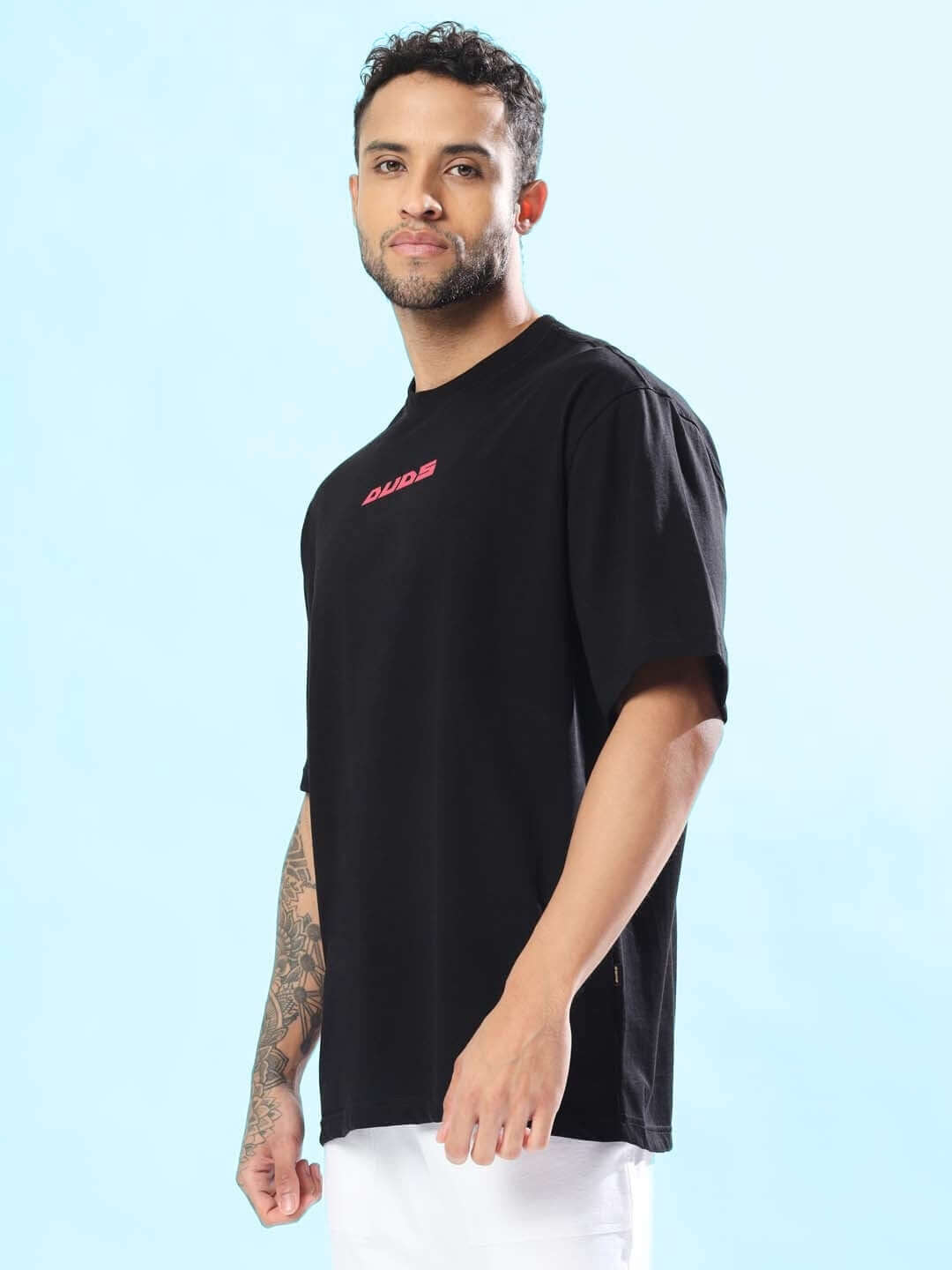 MAKE IT POSSIBLE OVER-SIZED T-SHIRT BLACK worn by model with tattoos standing sideways, showcasing the casual fit and style.