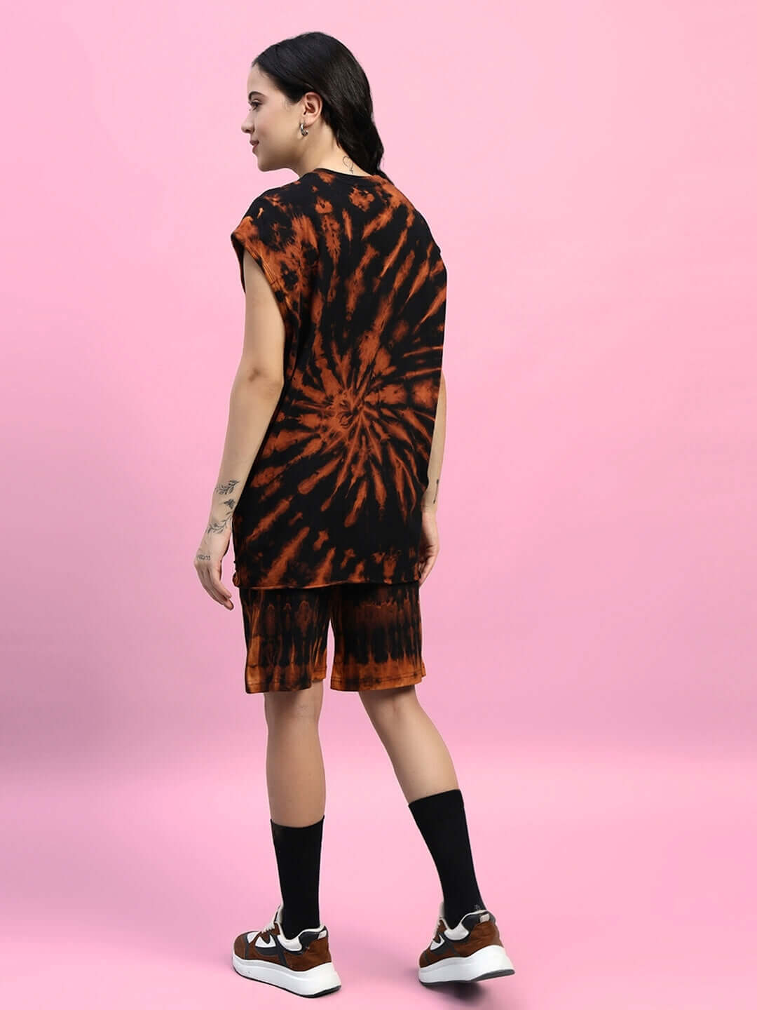 Woman wearing black tie-dye muscle tee and shorts co-ord set, standing against a pink background, showcasing back view.