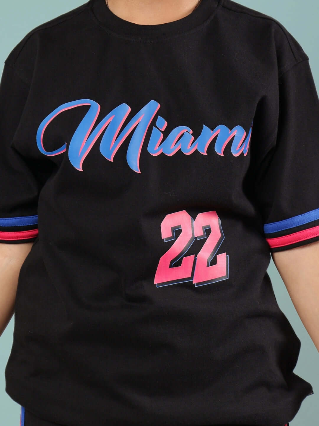 Child wearing a black oversized Miami t-shirt with blue and pink lettering and the number 22.