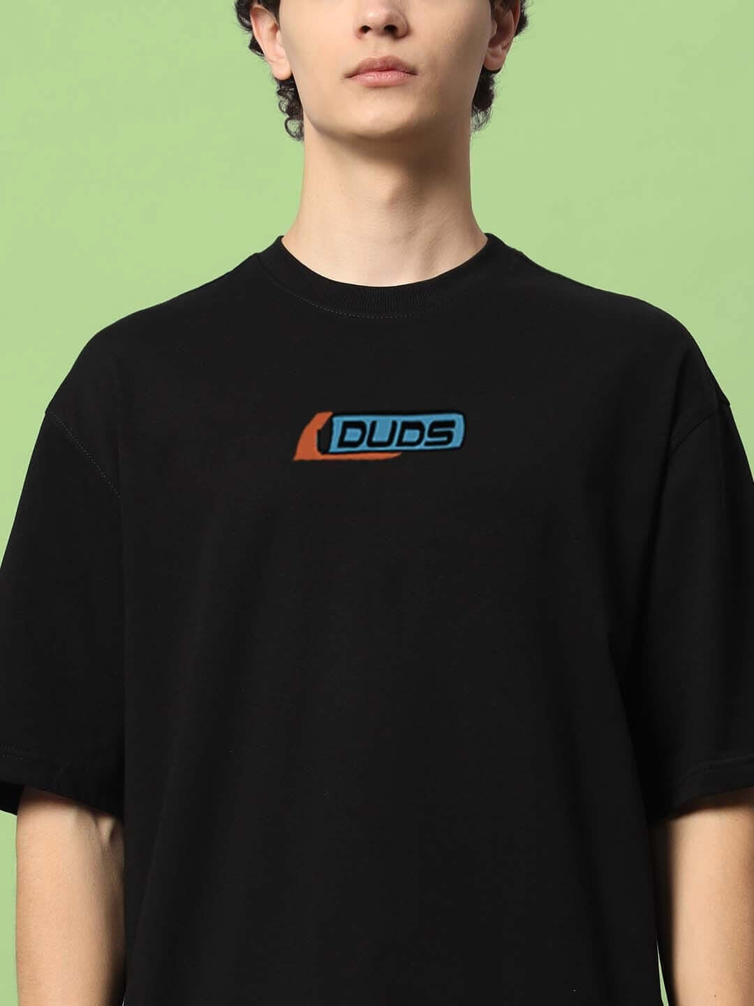 Man wearing ROBO SHARK OVER-SIZED T-SHIRT BLACK with DUDS logo, made from premium heavy gauge fabric, on green background.