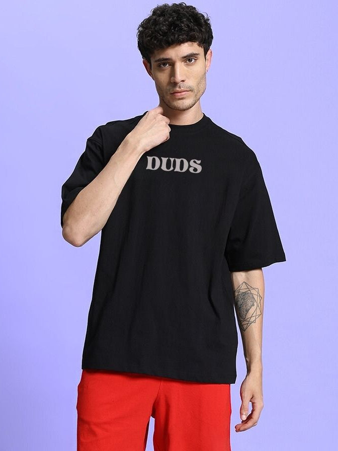 Model wearing FLORAL PRINT OVERSIZED T-SHIRT BLACK on purple background, showcasing design and fit.