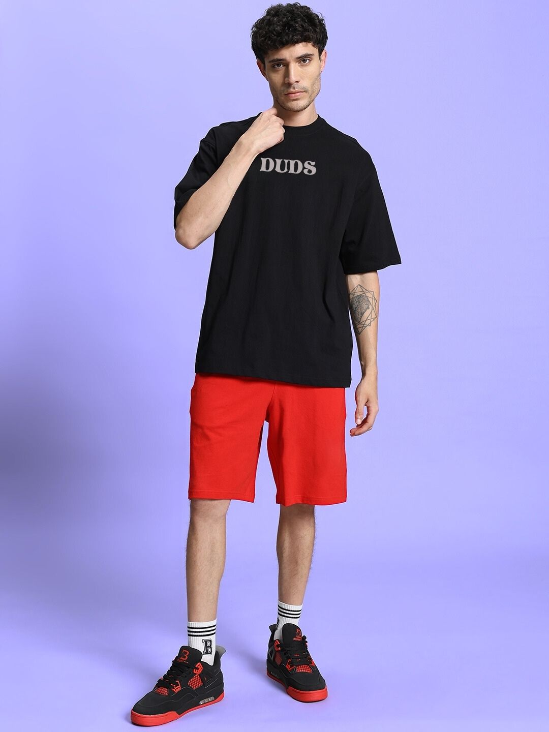 Man wearing FLORAL PRINTED SUMMER CO-ORD SET BLACK RED with black t-shirt and red shorts, standing against purple background.