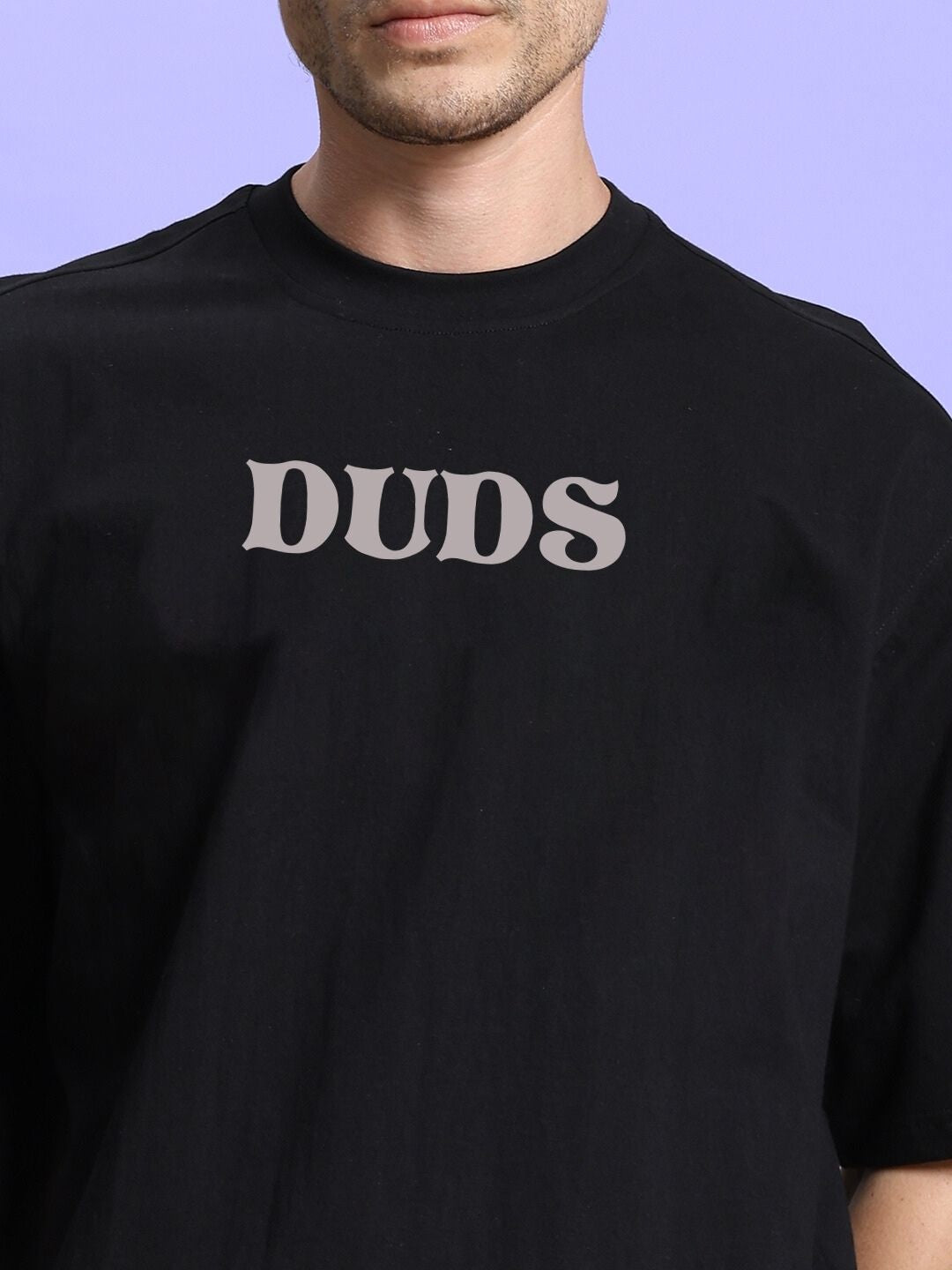 Man wearing a black T-shirt with 'DUDS' text print on the front, close-up view against a light purple background.