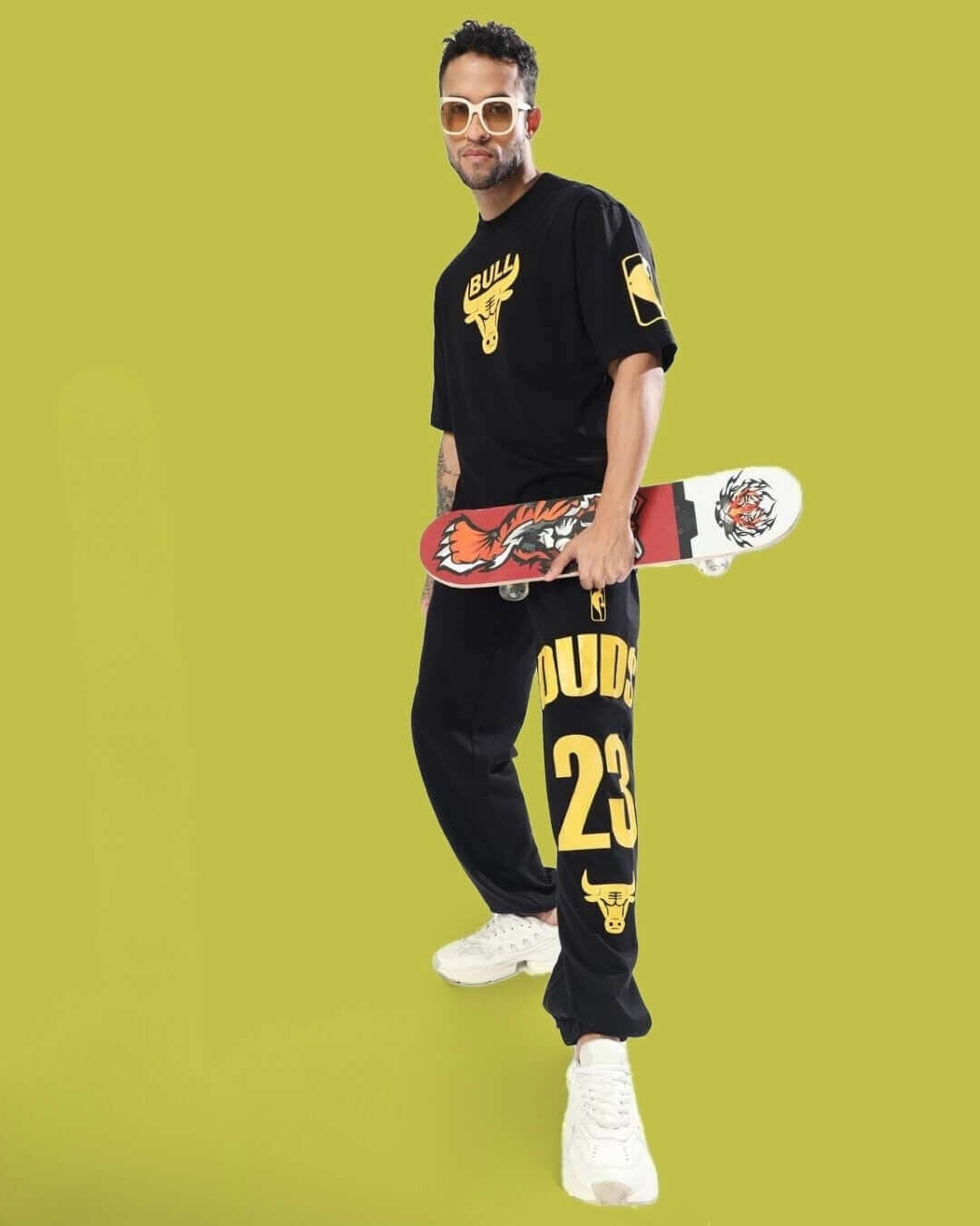 Person wearing black streetwear outfit with graphic prints, holding a skateboard