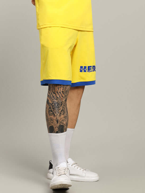 Yellow super hero summer shorts with blue trim, custom fit option available for prepaid orders, shown on model with tattooed leg.