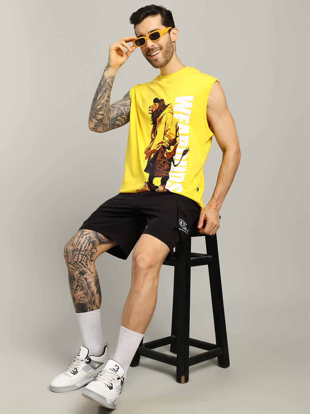 Man wearing yellow sleeveless shirt and black VEGA cargo shorts sitting on a stool.