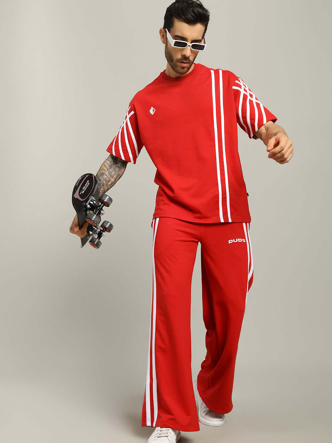 Model wearing United Stripe Over-Sized T-Shirt in red, made from premium cotton blend, holding a skateboard, showcasing sporty fashion.
