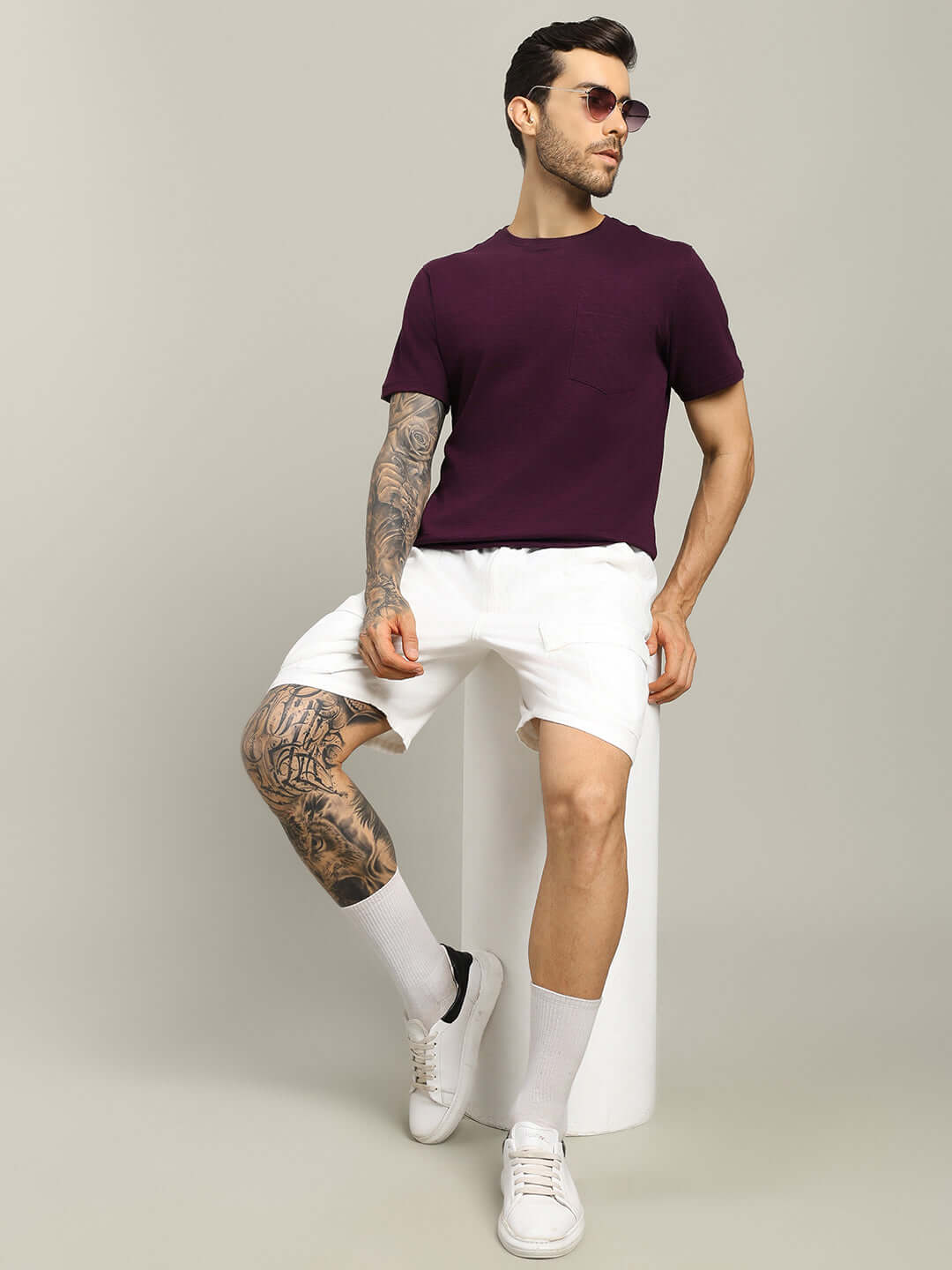 Man wearing JOY Regular Fit Purple T-shirt in premium heavy cotton, paired with white shorts and sunglasses, seated in a stylish pose.