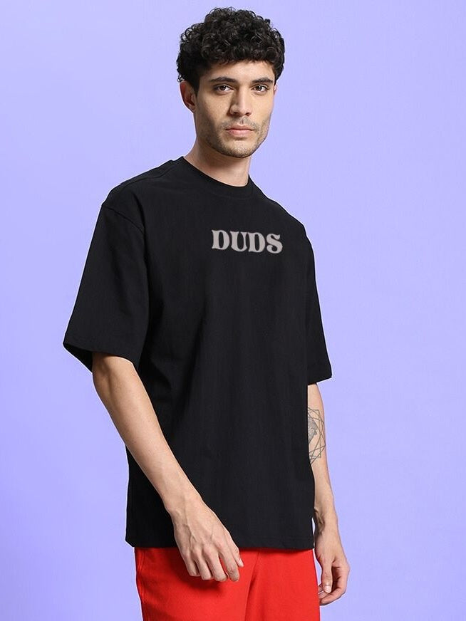 Man wearing a black FLORAL PRINT OVERSIZED T-SHIRT BLACK with DUDS text on front.