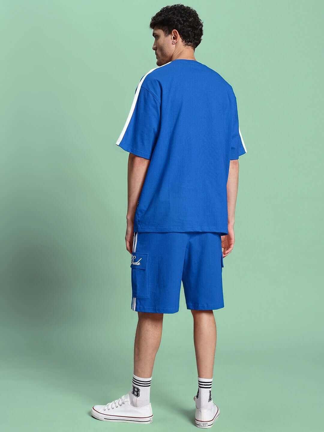 Man wearing Scotia Summer Co-Ord Set in blue, featuring premium cotton fabric, shot from the back against a green background.