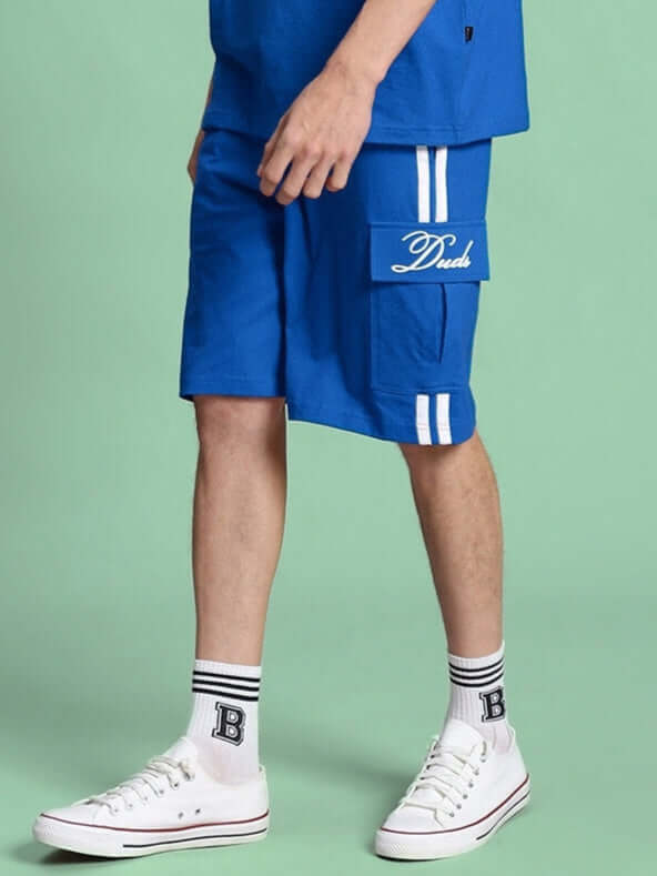 Man wearing blue Scotia Regular Fit Shorts with white sneakers, side pocket detail. Perfect for casual wear and customizable fit options.