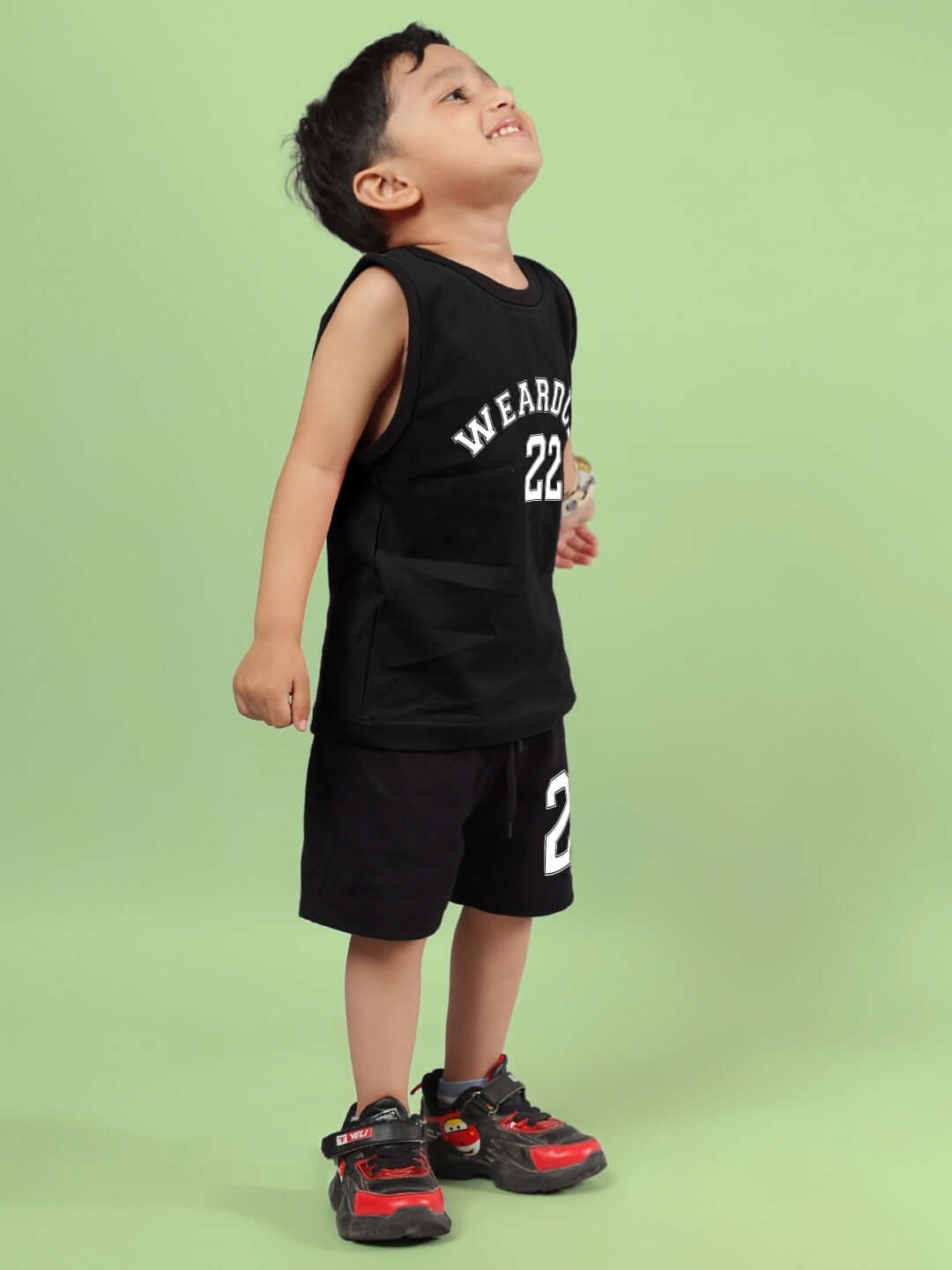 Young child wearing a black AMIGA co-ord set from DUDS suitable for boys and girls, featuring customized size options, against a green background.