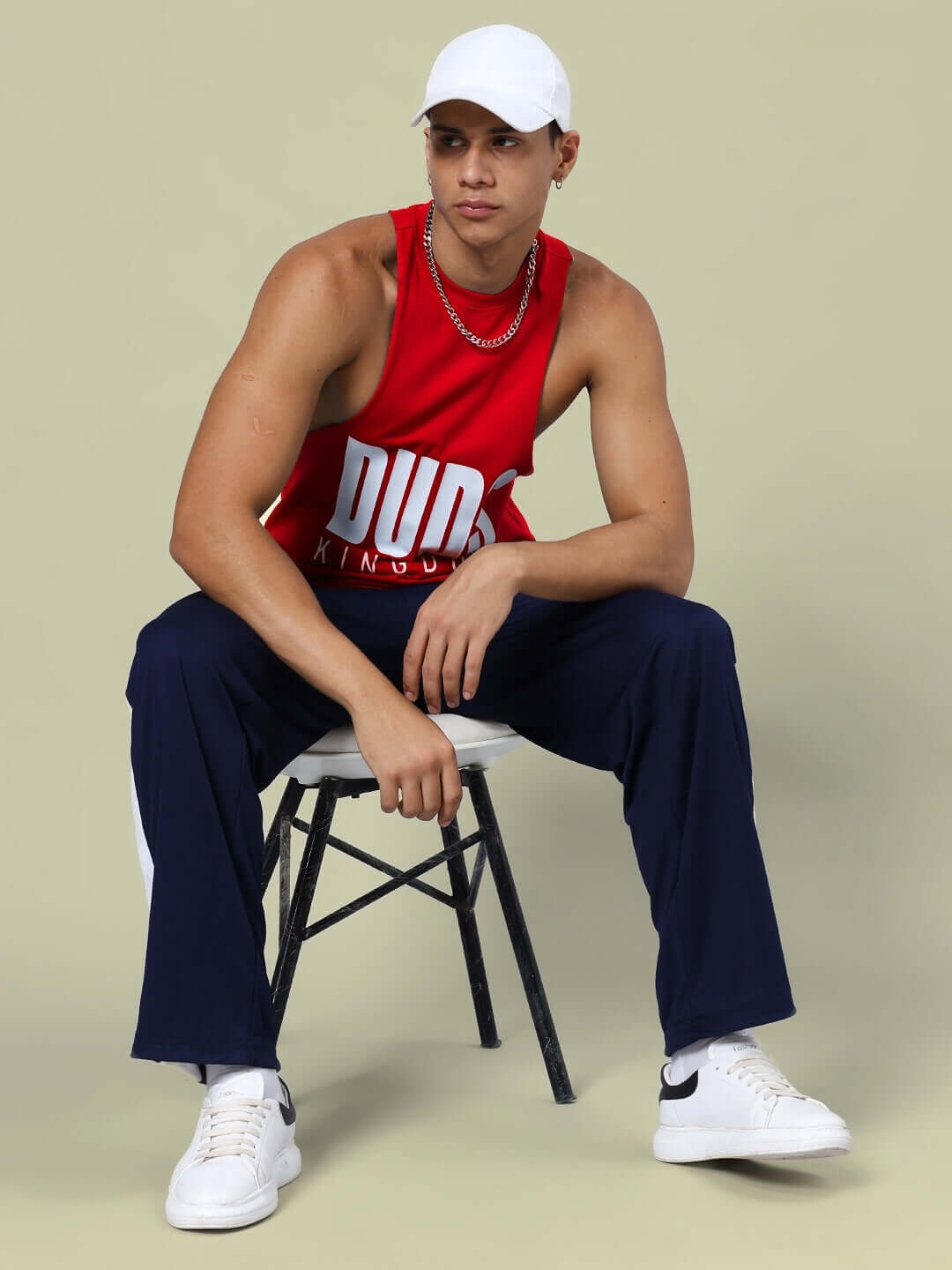 Model wearing DUDS KINGDOM red tank top with navy-blue joggers, sitting on a stool, showcasing unisex gym co-ord set.