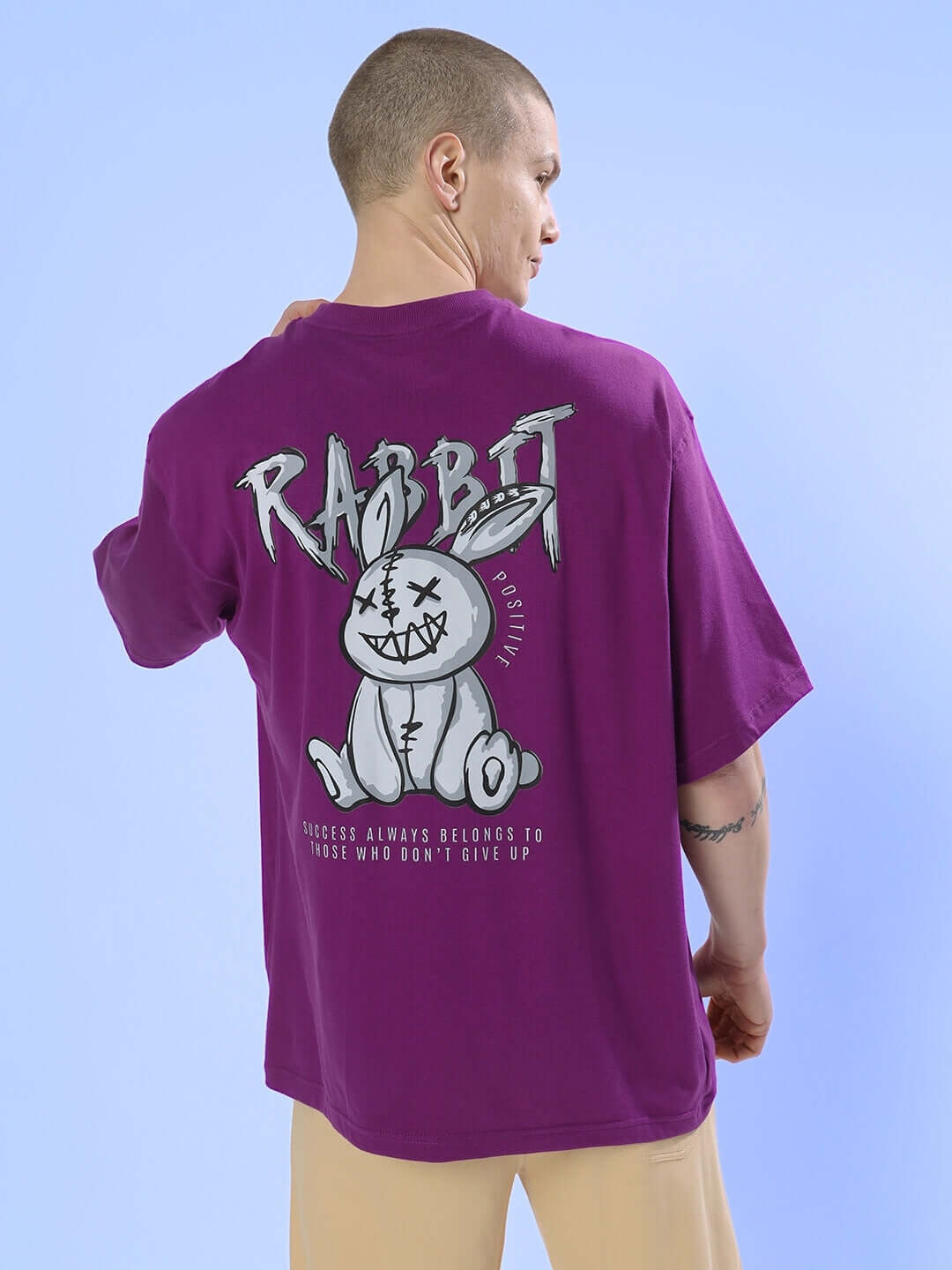 Man wearing Positive Rabbit Over-Sized T-Shirt Purple with playful graphic and text on back.
