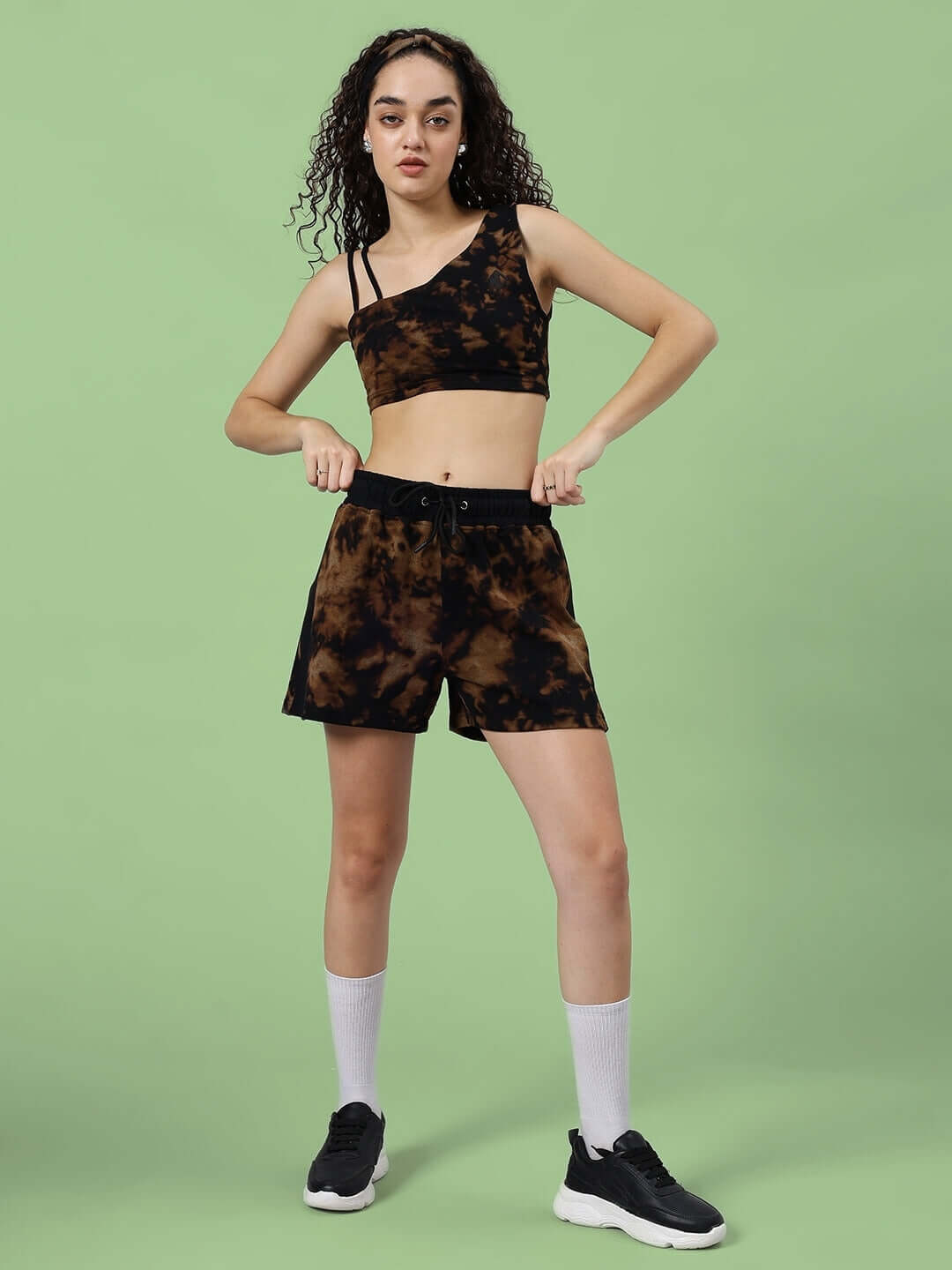 Woman wearing black tie-dye co-ord set, comprising a crop top and shorts, made from premium cotton blend fabric, on a green background.