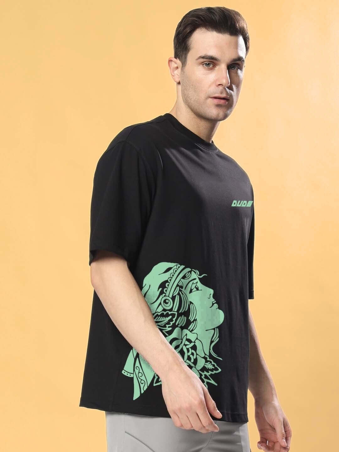 Person wearing KINNAUR OVER-SIZED T-SHIRT BLACK with custom fit option, DUDS brand fashion, featuring graphic design on front.