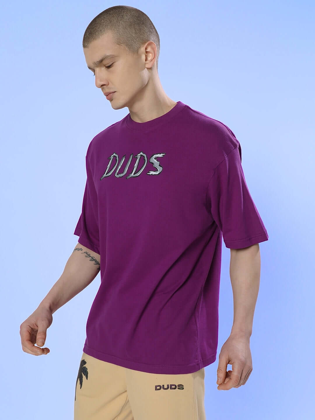 Man wearing POSITIVE RABBIT OVER-SIZED T-SHIRT PURPLE standing against blue background.