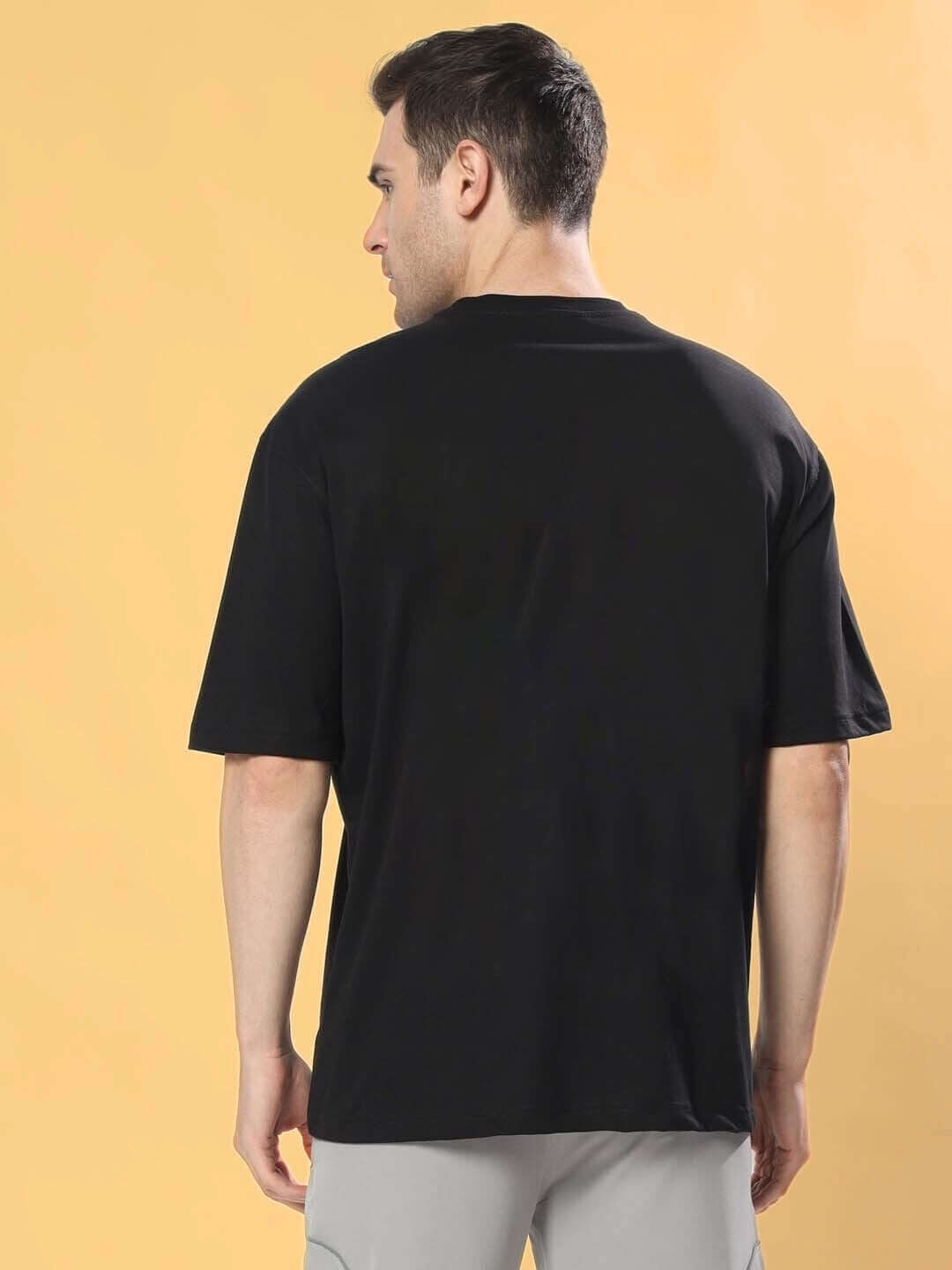 Man wearing KINNAUR OVER-SIZED T-SHIRT BLACK, shown from the back.
