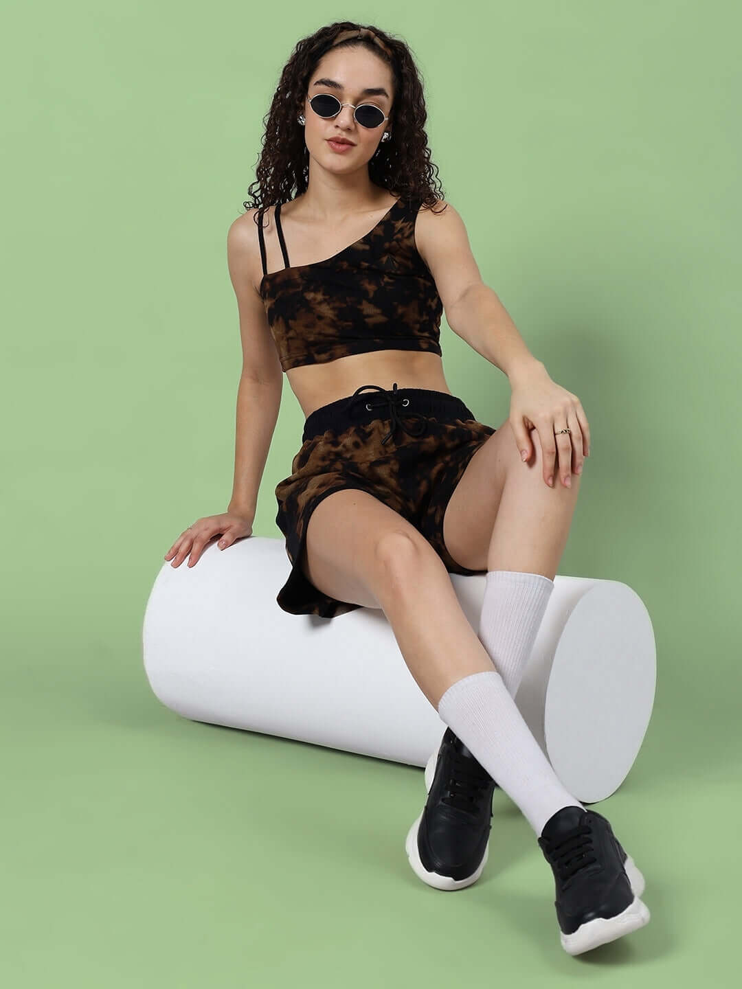 Model wearing black women's tie-dye co-ord set, featuring crop top and shorts, made from premium cotton fabric on green backdrop.
