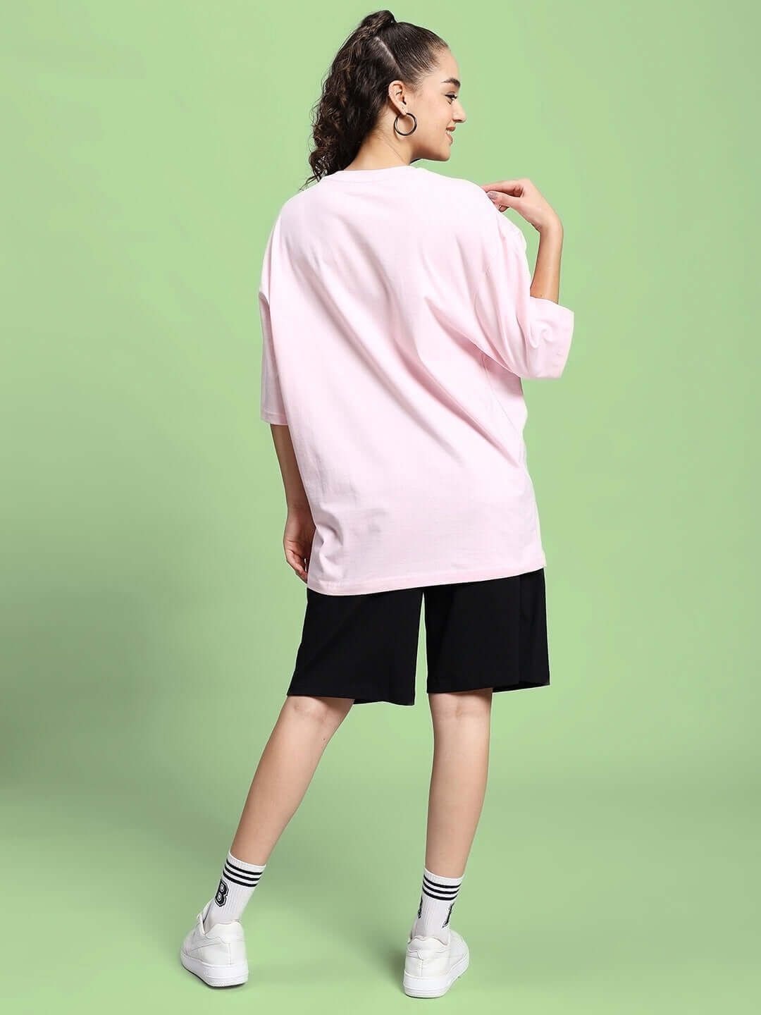 Woman wearing a pink tee and black shorts from the Be Kind Summer Co-Ord Set, standing against a green background.