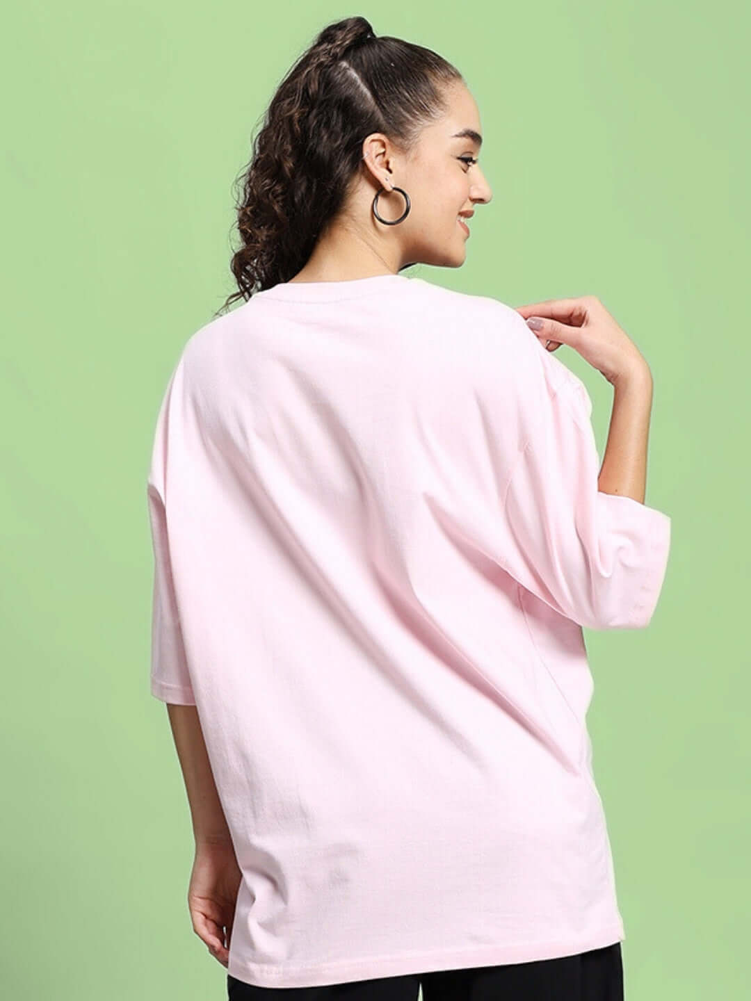 Back view of a woman wearing a pink oversized 'Be Kind' t-shirt made from premium cotton French terry fabric.