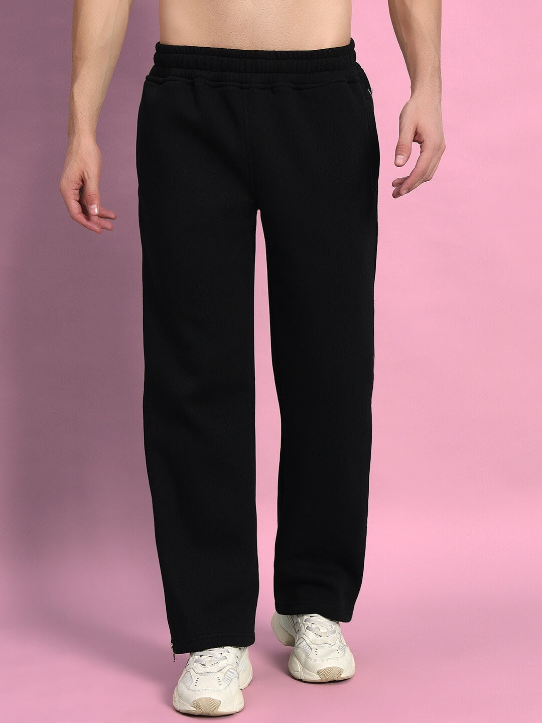 Black fleece jogger pants with reflector detailing, shown on a model against a pink background.