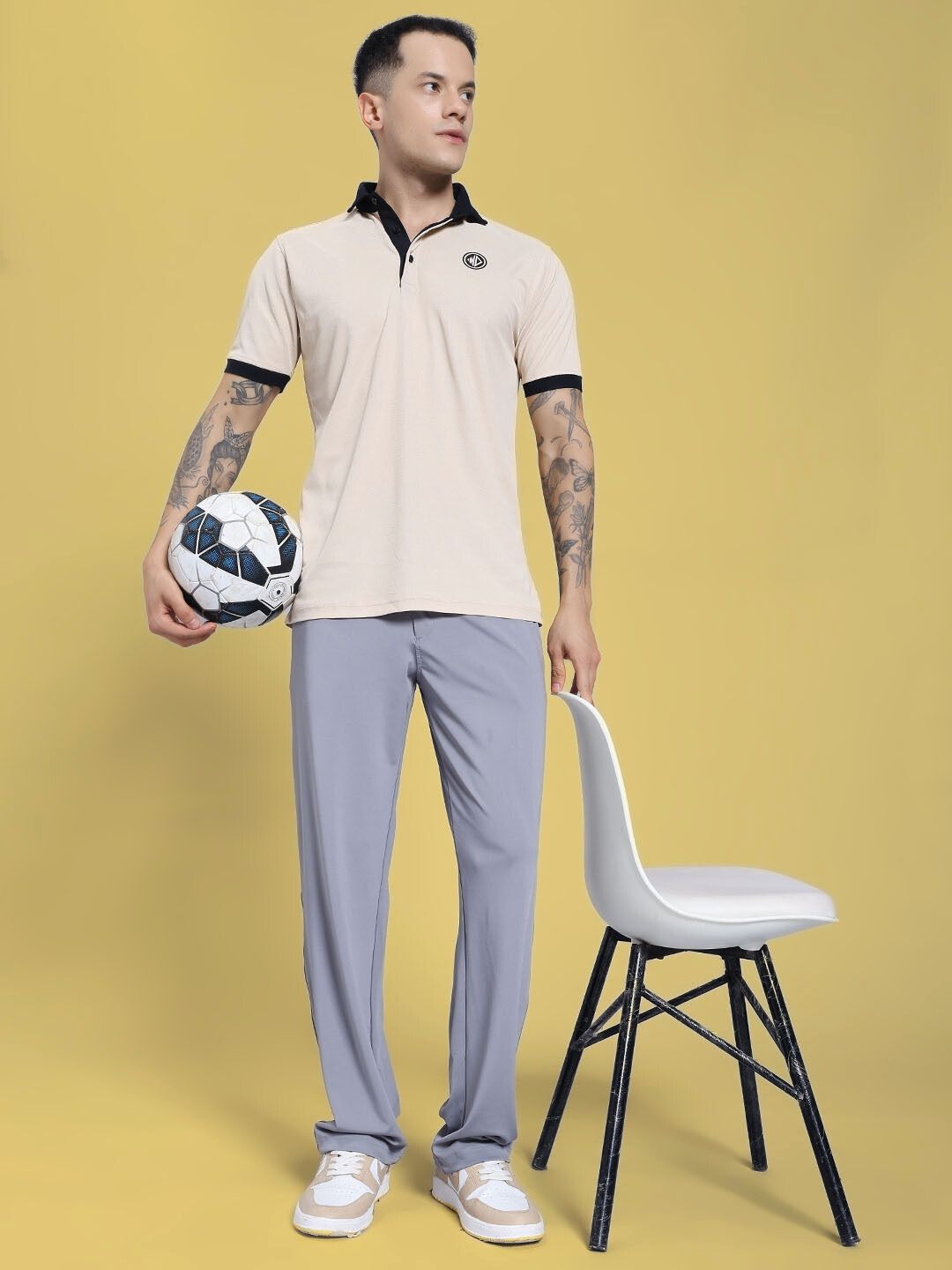 Man wearing REVOXX RELAXED FIT JOGGER GREY standing with a soccer ball and chair against a yellow background.