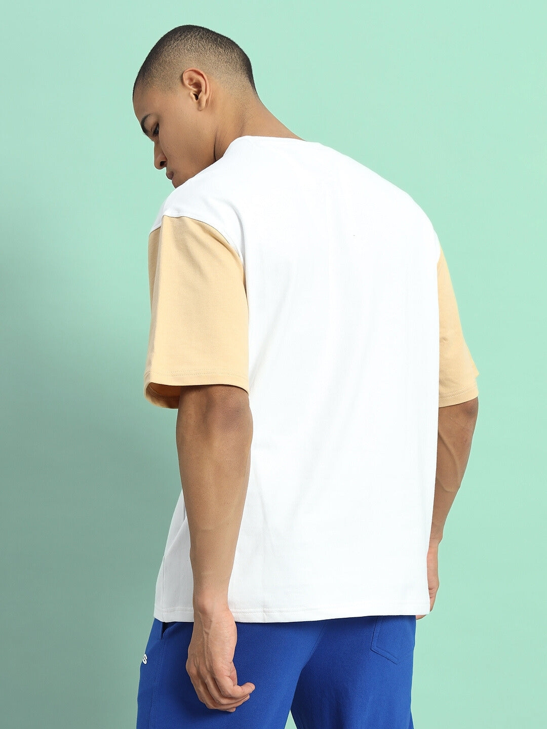 Model wearing FRESCO COLOR BLOCKED OVERSIZED T-SHIRT WHITE BEIGE with premium cotton fabric, back view against a mint green background.