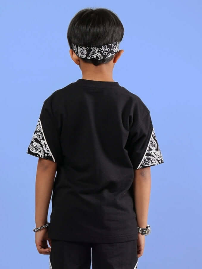 Child wearing CALVIN oversized black t-shirt with bandana pattern sleeves, viewed from the back.