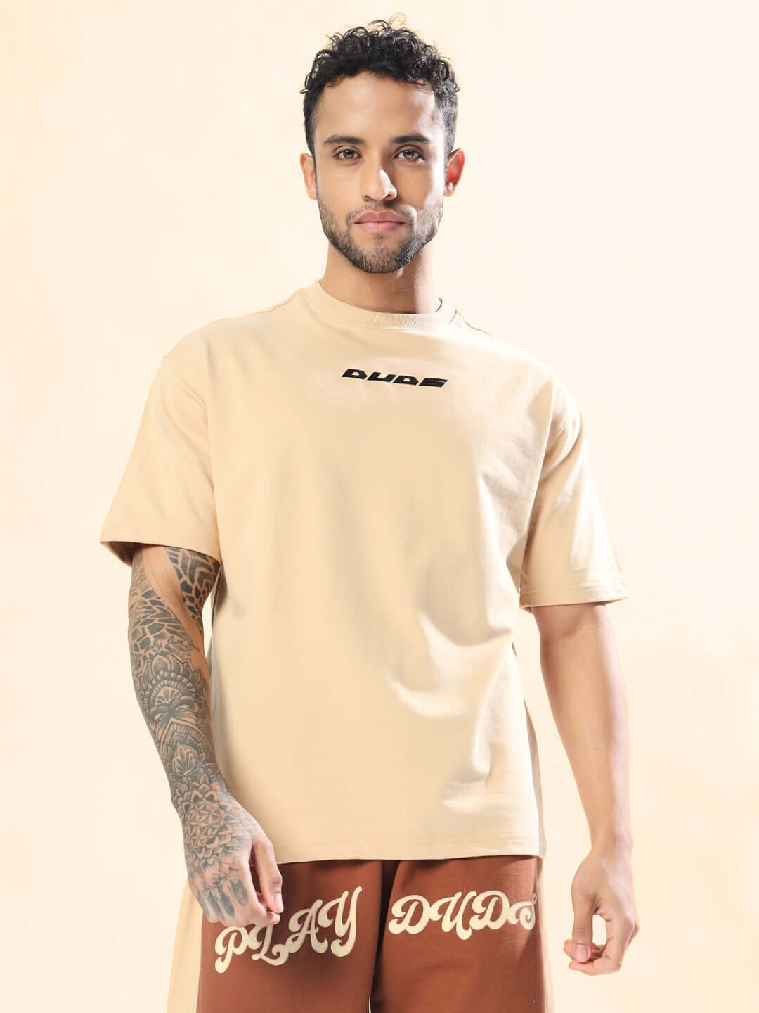 Model wearing MORE 777 OVER-SIZED T-SHIRT BEIGE made of premium heavy gauge fabric, 97% cotton, 3% elastane in a casual setting.