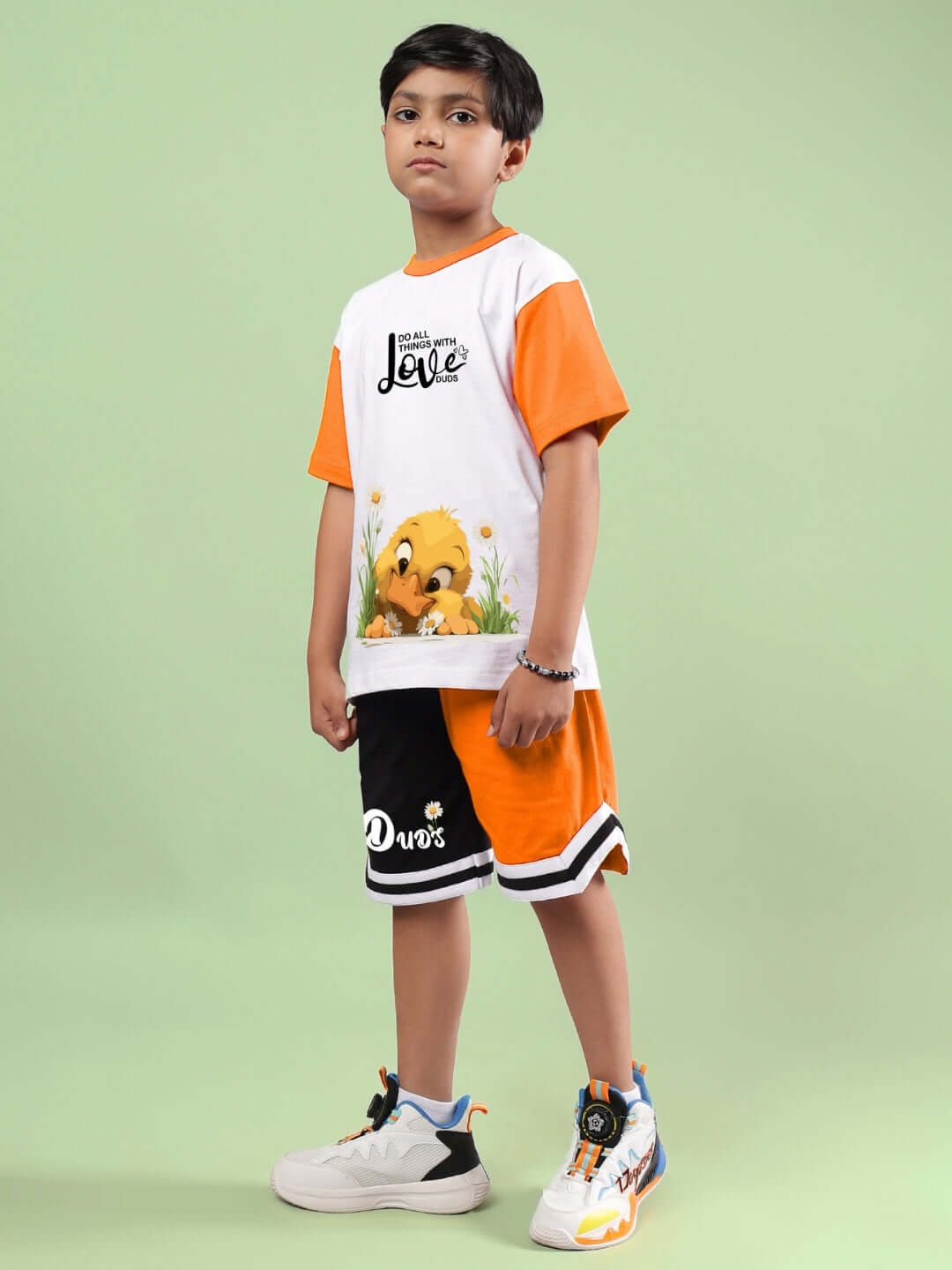 Boy wearing white and orange friendship bucket co-ord set by DUDS, featuring an animal print and sporty sneakers against a light green background.