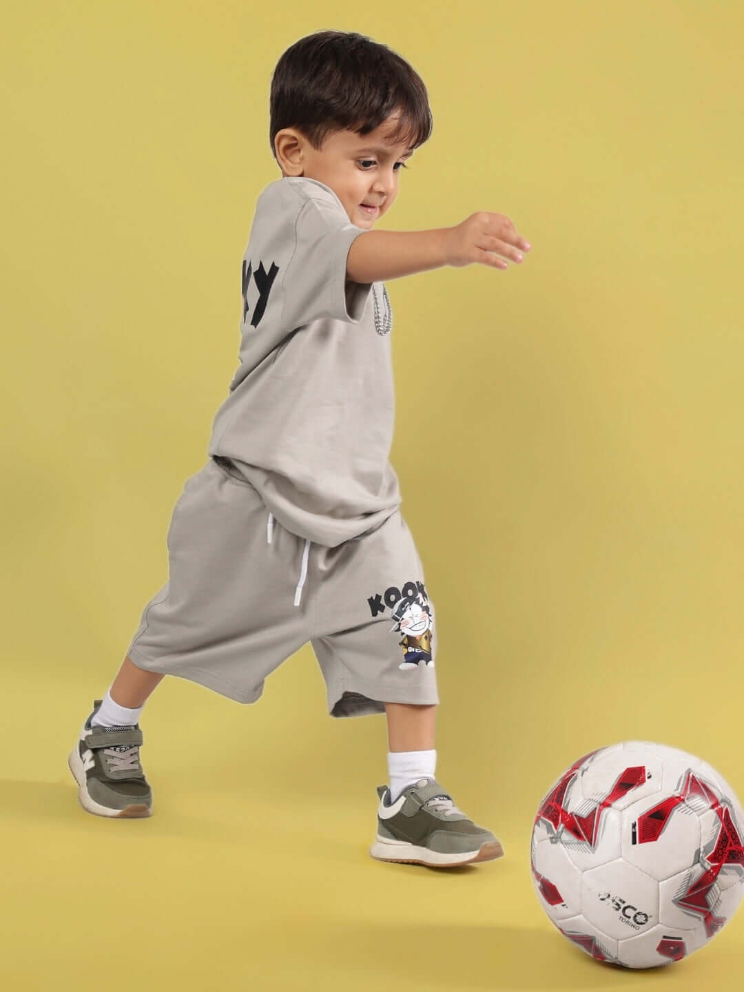 Child playing with a soccer ball wearing a grey KOOKY t-shirt and shorts, suitable for both boys and girls. Custom fit available.