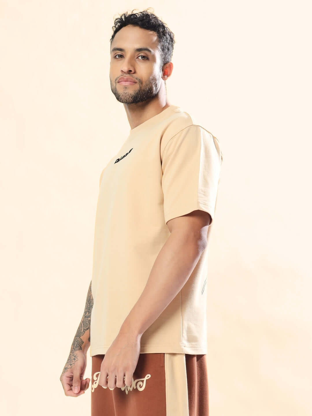 Man wearing MORE 777 OVER-SIZED T-SHIRT BEIGE, made from premium heavy gauge fabric with 97% cotton and 3% elastane, stylish design.
