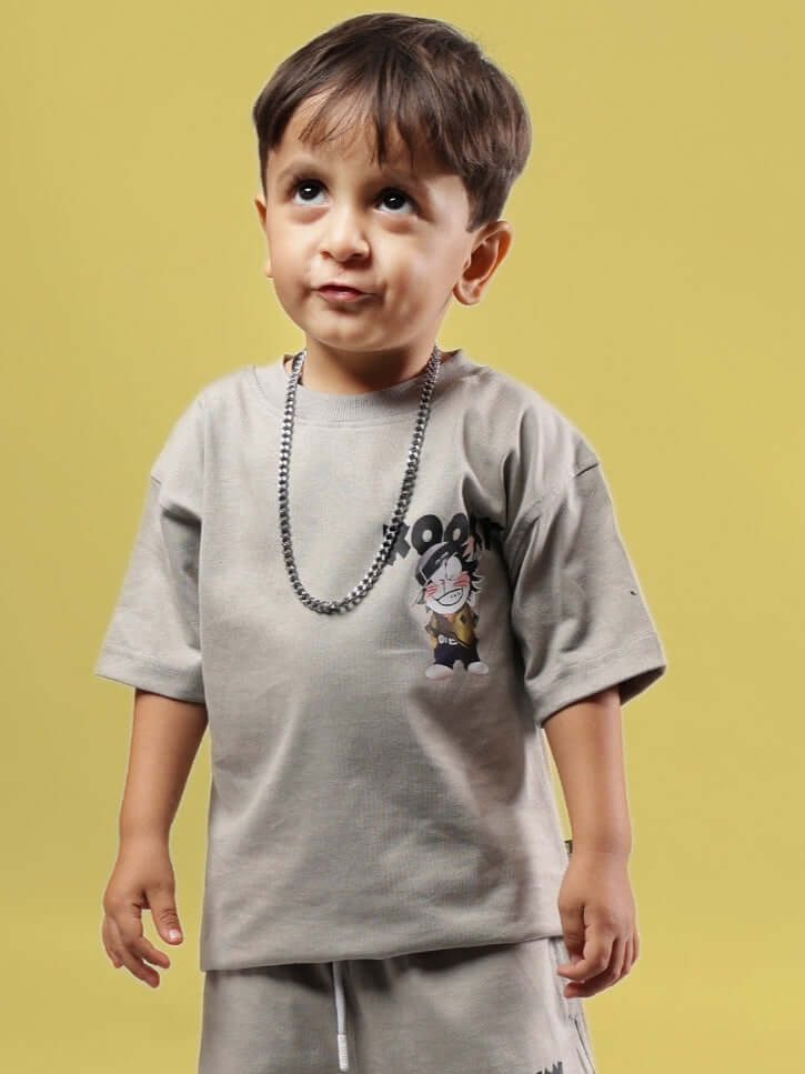 Young child wearing a grey KOOKY T-shirt for boys and girls, featuring a playful design, standing against a yellow background.