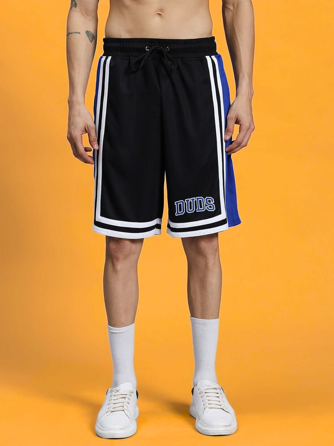 Black and blue colorblock sports shorts with white stripes and 'DUDS' embroidery, worn by model, set against an orange background.