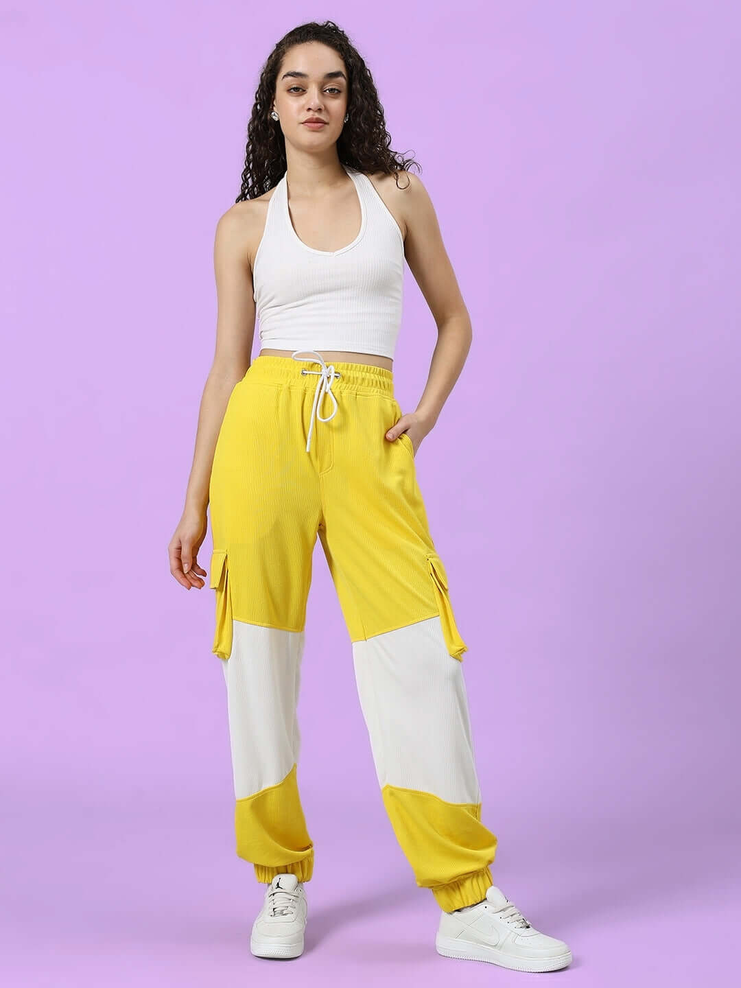 Model wearing yellow and white relaxed fit joggers, part of the women's custom fit collection by DUDS, with purple background.