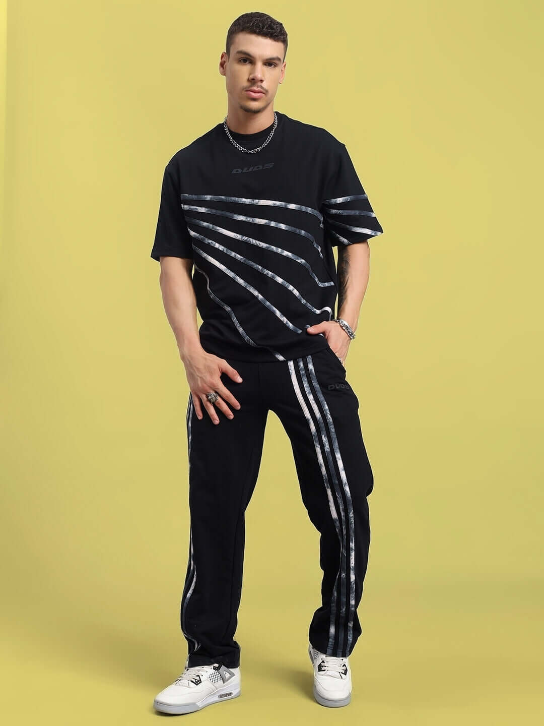 A model wearing the FLICKER JOGGER in black, featuring a contemporary design for custom fit by DUDS, standing against a yellow background.