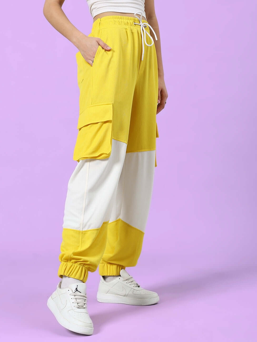 Model wearing yellow and white women's relaxed fit joggers by DUDS, featuring cargo pockets, elastic waistband, and customizable sizing.