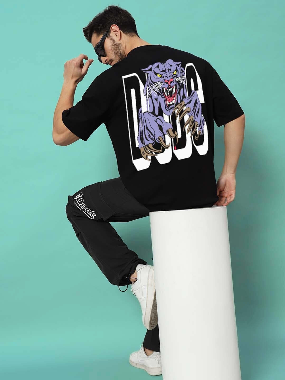 Man wearing DUDS PANTHER OVER-SIZED T-SHIRT BLACK sitting on a white block