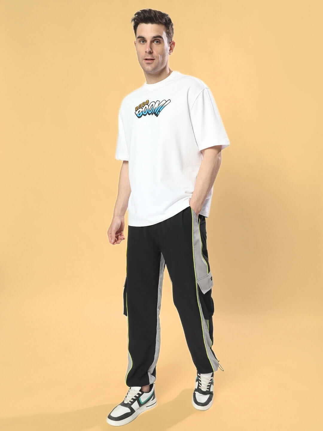 Model wearing BOOM BUNNY OVER-SIZED T-SHIRT WHITE with graphic design, styled with black and gray pants on a yellow background.