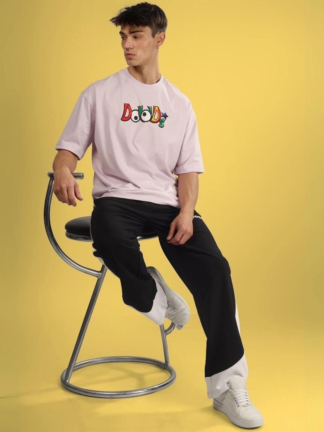 Man wearing DUDS MONSTER OVER-SIZED T-SHIRT PALE PINK seated on a chair with a yellow background