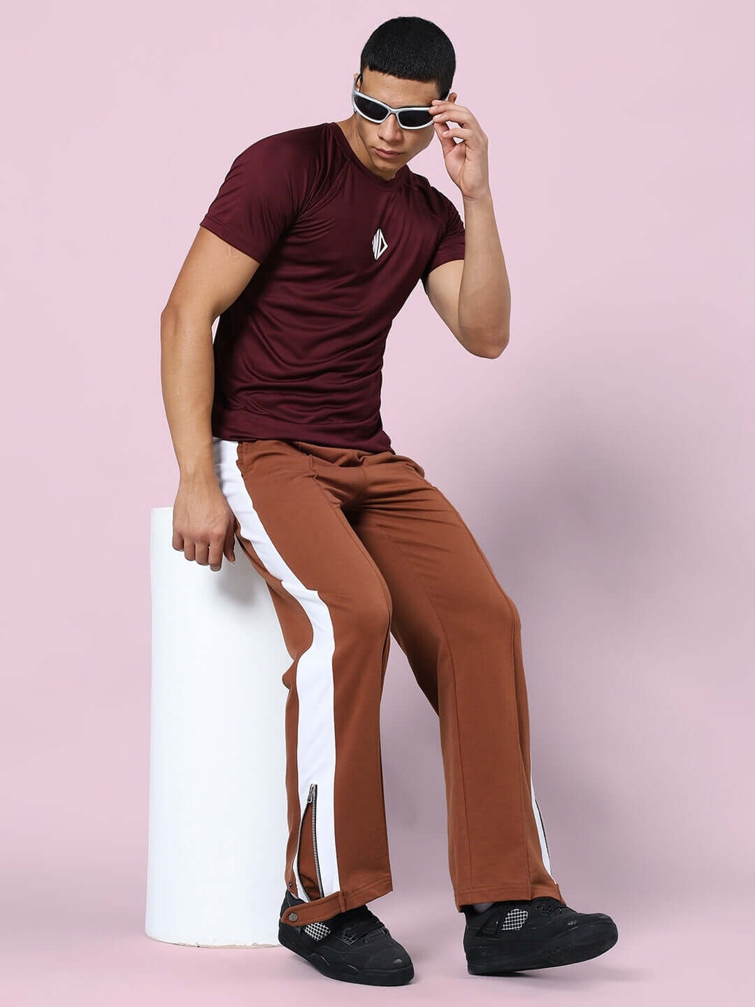 Model wearing Wonder Slit Zipper Joggers in brown, seated stylishly in sunglasses, highlighting the casual and trendy fashion look.