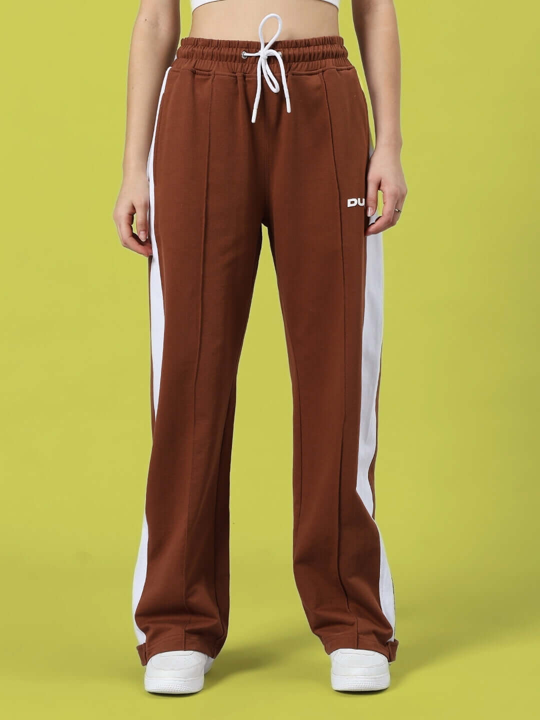 Model wearing Women's Wonder Slit Zipper Joggers in brown with side stripes, standing against a yellow background.